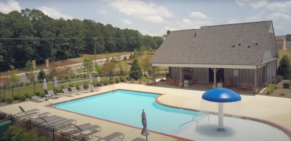Community pool with a blue mushroom fountain, lounge chairs, and a covered pool house on a summer afternoon