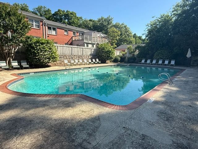 Kidney-shaped pool at a brick apartment community with lounge chairs along the far edge and trees overhead