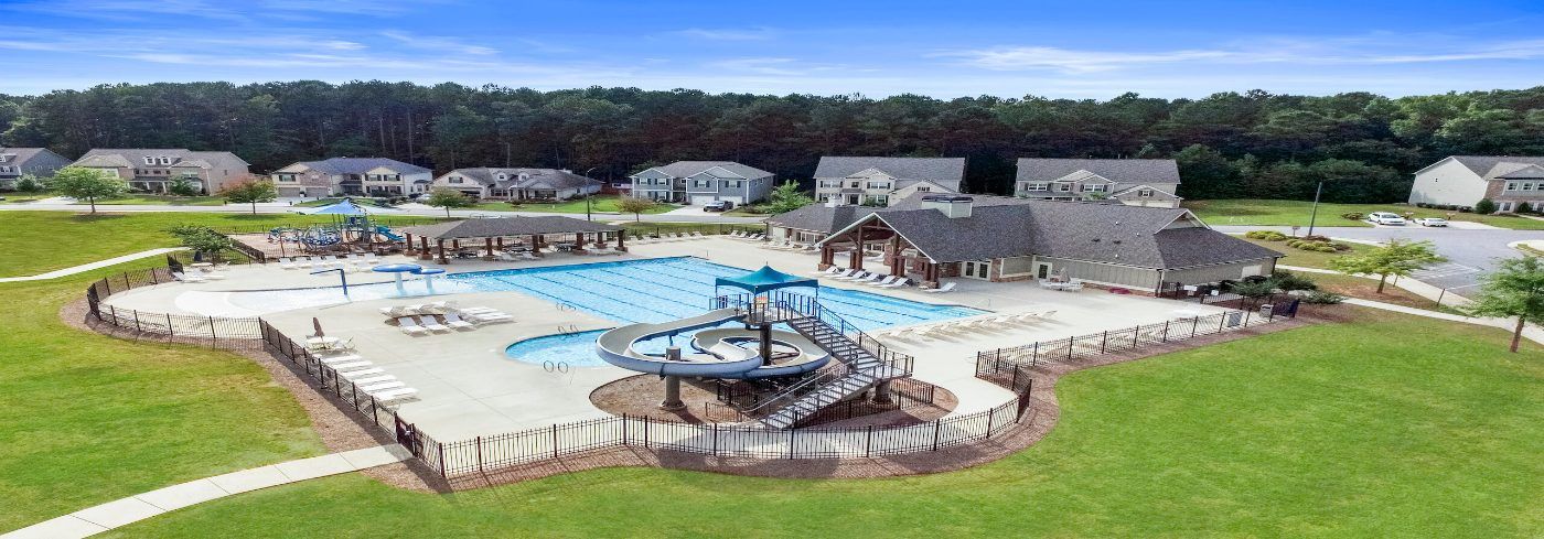 Aerial view of a large community pool with a water slide, a zero-entry area, and a clubhouse, surrounded by townhomes and lawn