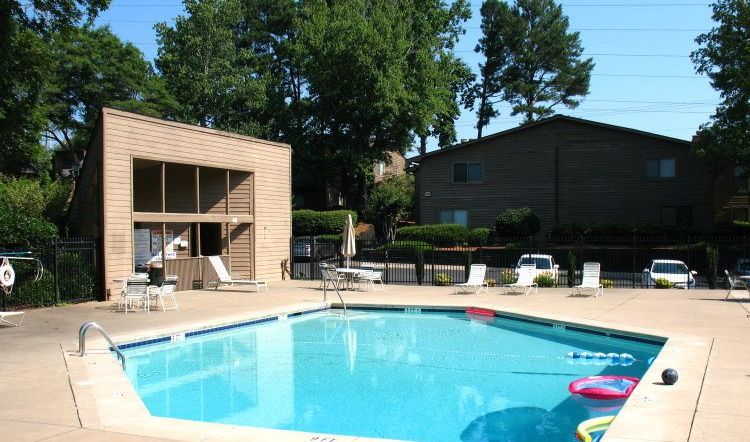 Rectangular community pool with a wood-sided pool house and an iron fence